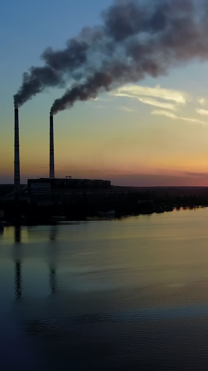 Factory Pipe Polluting Air. Pollution of the environment by the plant near river at evening sky Vertical video