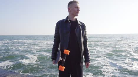 Der-Junge-Mann-Hält-Sein-Longboard-Am-Meer