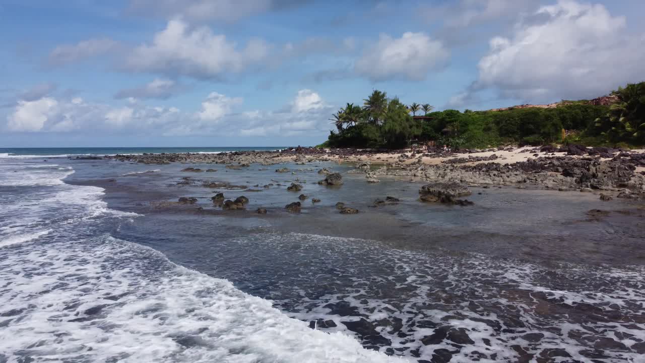 Plan rapproché de piscines naturelles sur une plage vers une jeune fille marchant sur le sable.