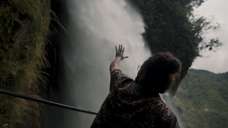 macho con la mano alcanzando hacia la cascada de pailon del diablo en baños de agua santa, ecuador - primer plano