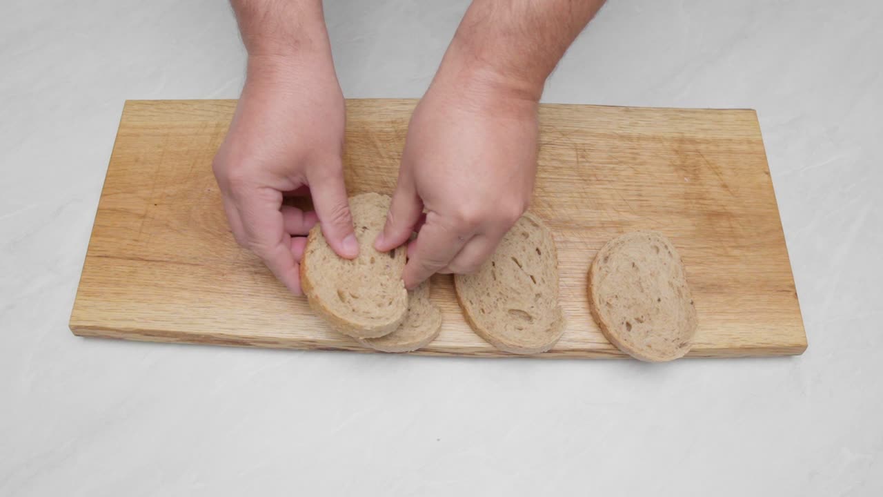 Hands arranging sliced bread on a wooden board as part of a food preparation process