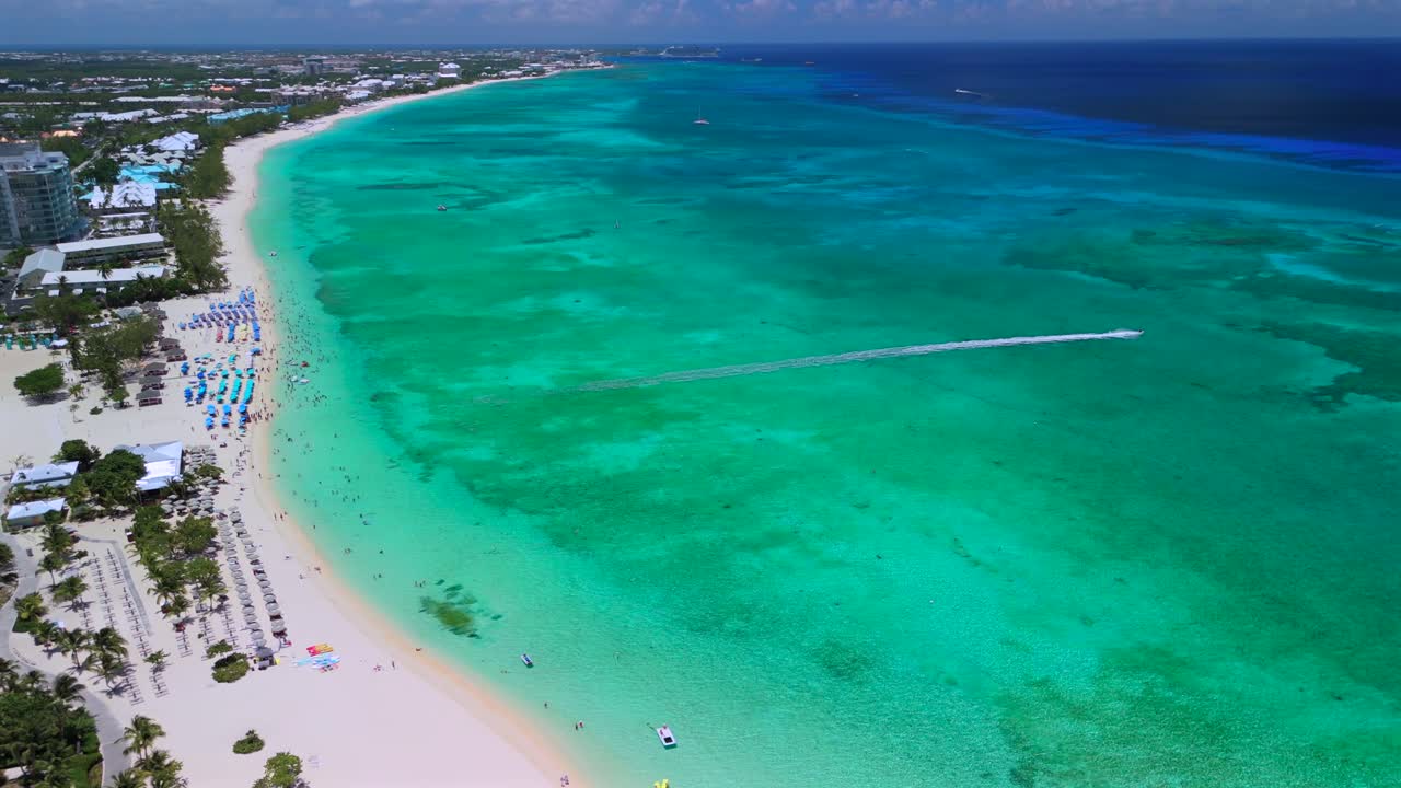 Aerial pull-back ascend shows Seven Mile Beach’s white sand and blue Caribbean water