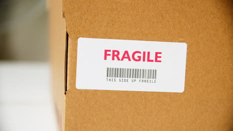 manos aplicando una etiqueta adhesiva frágil en una caja de cartón con código de barras de este lado hacia arriba