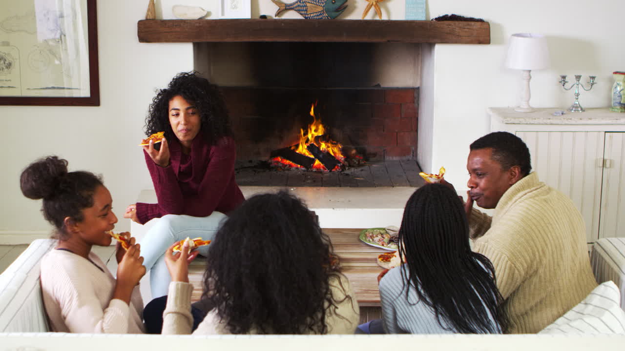familia sentada en el sofá en el salón al lado del fuego abierto comiendo pizza
