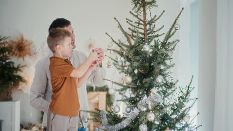 smiling little boy and dad put baubles on the tree