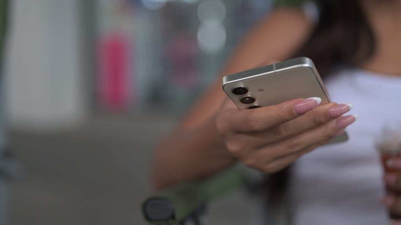 Detail ženské ruky držící a používající chytrý telefon venku s prostorem pro text.