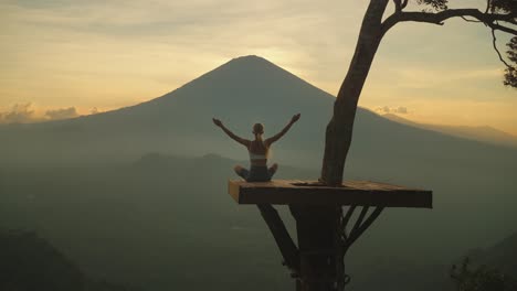 woman lifting arms on platform doing yoga in front of majestic mount agung, sunset