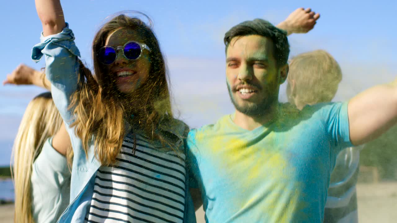 retrato de una pareja feliz cubierta de colorido polvo bailando en el festival de holi. la gente en el fondo se divierten lanzando polvo de holi