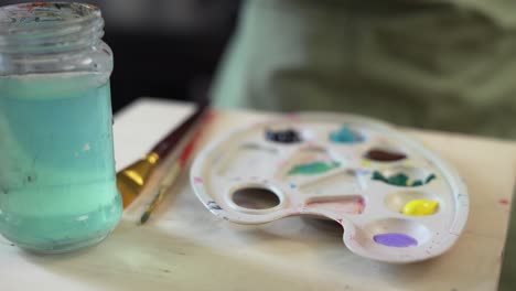 woman hand cleaning in water paintbrush with acrylic paints on background