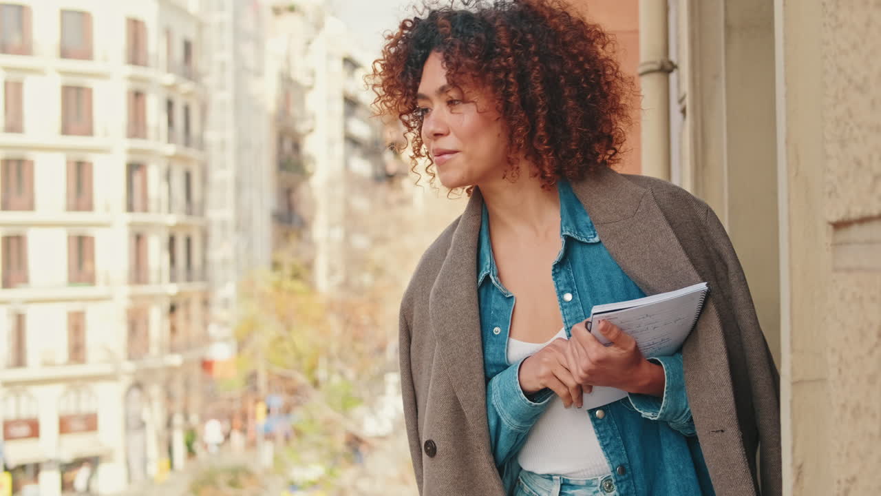 Thoughtful Young Woman with Curly Hair Looking Out from City Balcony