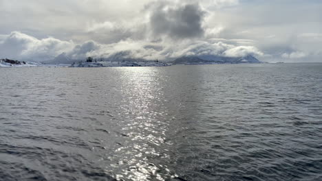 Panning-shot-of-the-ocean-with-a-pillar-of-clounds-and-snow-covered-landscape-in-the-background