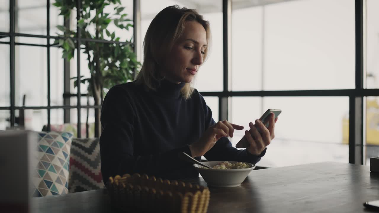 una mujer rubia atractiva usa un teléfono inteligente en un café. una mujer está hablando con amigos y colegas