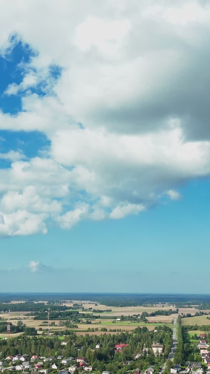 Vertical tilt view over Talsi neighborhood houses beneath a bright blue sky with fluffy clouds