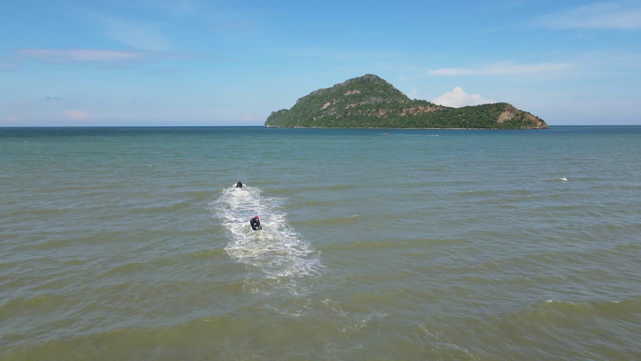 섬을 향해 속도를 내며 중간에서 서로를 따라가는 두 개의 제트 스키, 공중 고정 영상