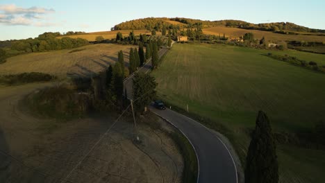 cars drive along winding asphalt road across farmland fields at golden hour in tuscany