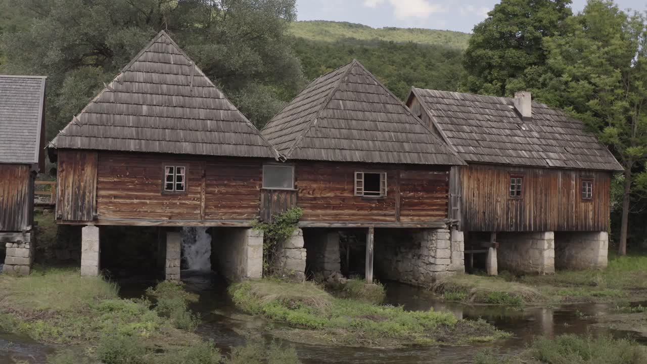 Drone shot of a stream flowing through a scenic landscape, with cozy cottages on the water