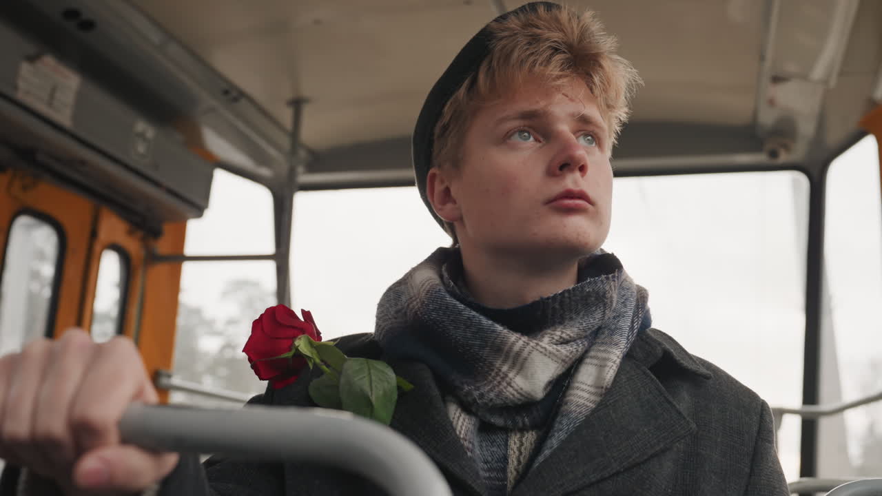 Sognatore bianco speranzoso sull'autobus, rosa. Giovane creatore bianco romantico che tiene una rosa al petto, occhi puntati sull'orizzonte lontano, sciarpa e berretto accoglienti, interni vintage caldi, desiderio silenzioso e delicato ottimismo