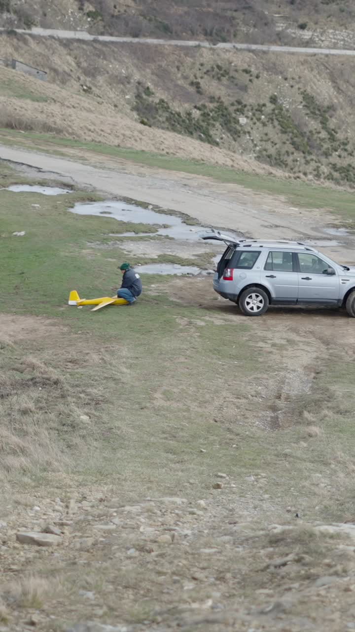 A man with a yellow model airplane next to a car