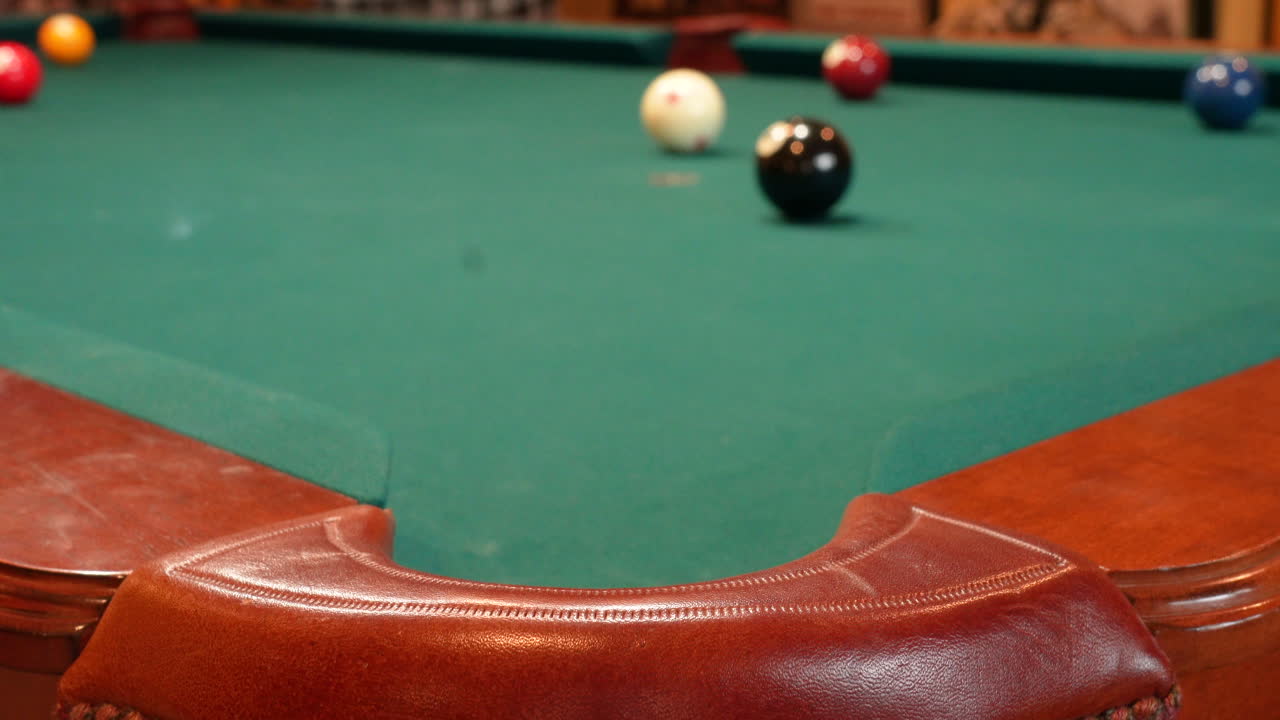 Person Playing Pool Walking up to and Shooting 8 Ball into Corner Pocket after Practice Strokes using Cue Ball, Open Bridge Hand with Wooden Cue Stick, Solid Black Ball and Green Felt or Cloth
