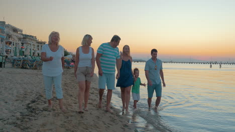 gran familia feliz y divertida camina por la playa en el fondo del atardecer de pireo, grecia