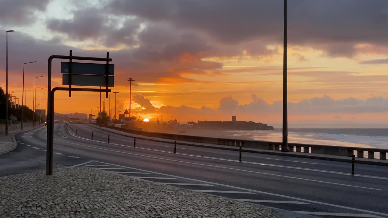 amplia vista de nubes naranjas en movimiento sobre la ciudad y la playa en cascais sobre la calle con autos en movimiento durante el amanecer
