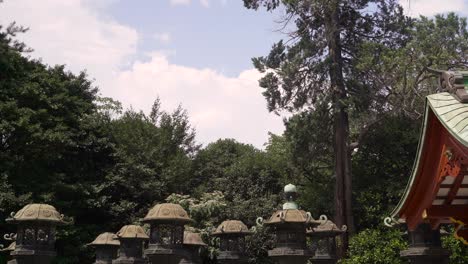 Typical-Japanese-stone-pillars-and-red-shrine-building-in-Japanese-temple-against-blue-sky-with-clouds