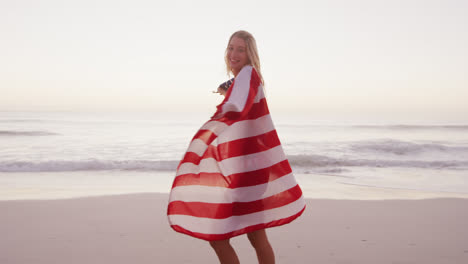 Mujer-Caucásica-Sosteniendo-Y-Ondeando-Una-Bandera-Estadounidense-En-La-Playa.