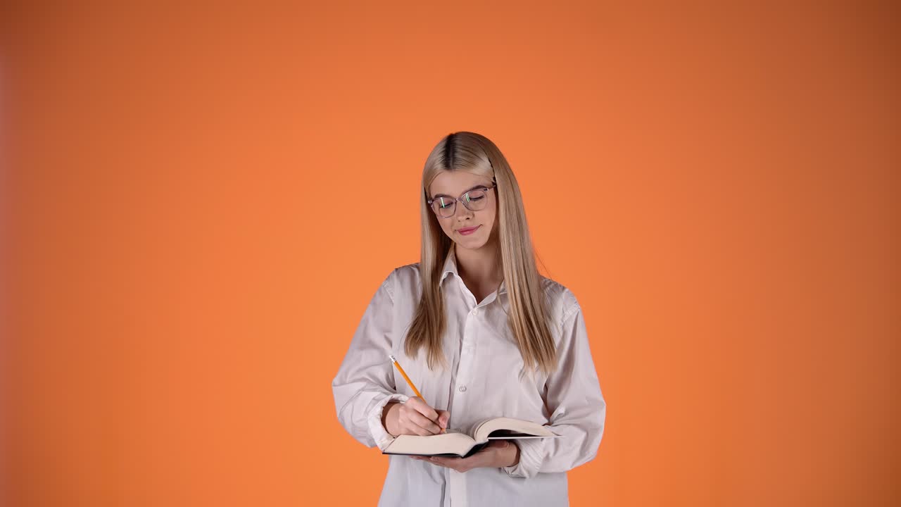 Attraente donna bionda riflette su una domanda e trova la risposta, prendendo appunti su un quaderno di carta, scatto in studio