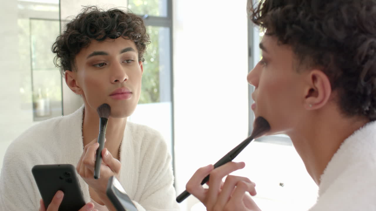 Applying makeup, young non binary person using brush and looking in mirror