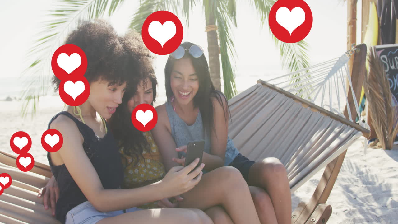 animación de iconas digitales de amor de corazón rojo sobre amigas en hamaca con teléfono inteligente en la playa