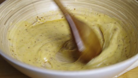 Adding-water-and-mixing-caesar-salad-sauce-with-wooden-cooking-spoon-inside-deep-bowl