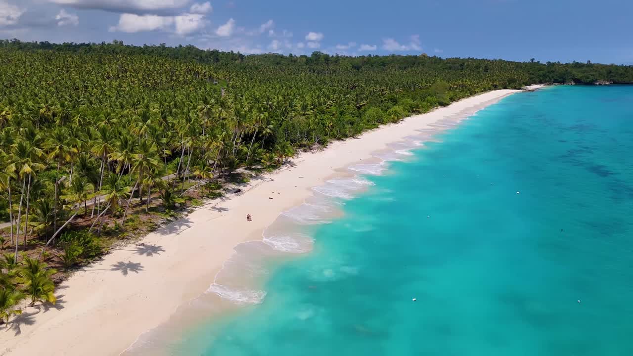 Video drone 4K con panoramica che mostra una coppia che cammina lungo una spiaggia tropicale di sabbia bianca nelle Isole Banggai a Sulawesi, Indonesia. Questa è Mandel Beach, un paradiso tropicale vicino a Luwuk.