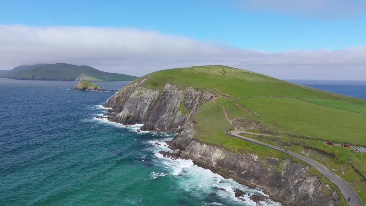 Scogliere frastagliate che incontrano l'Oceano Atlantico nella penisola di Dingle. La scena cattura l'ampio paesaggio verde e le acque di un blu profondo. Perfetto per contenuti di viaggio.