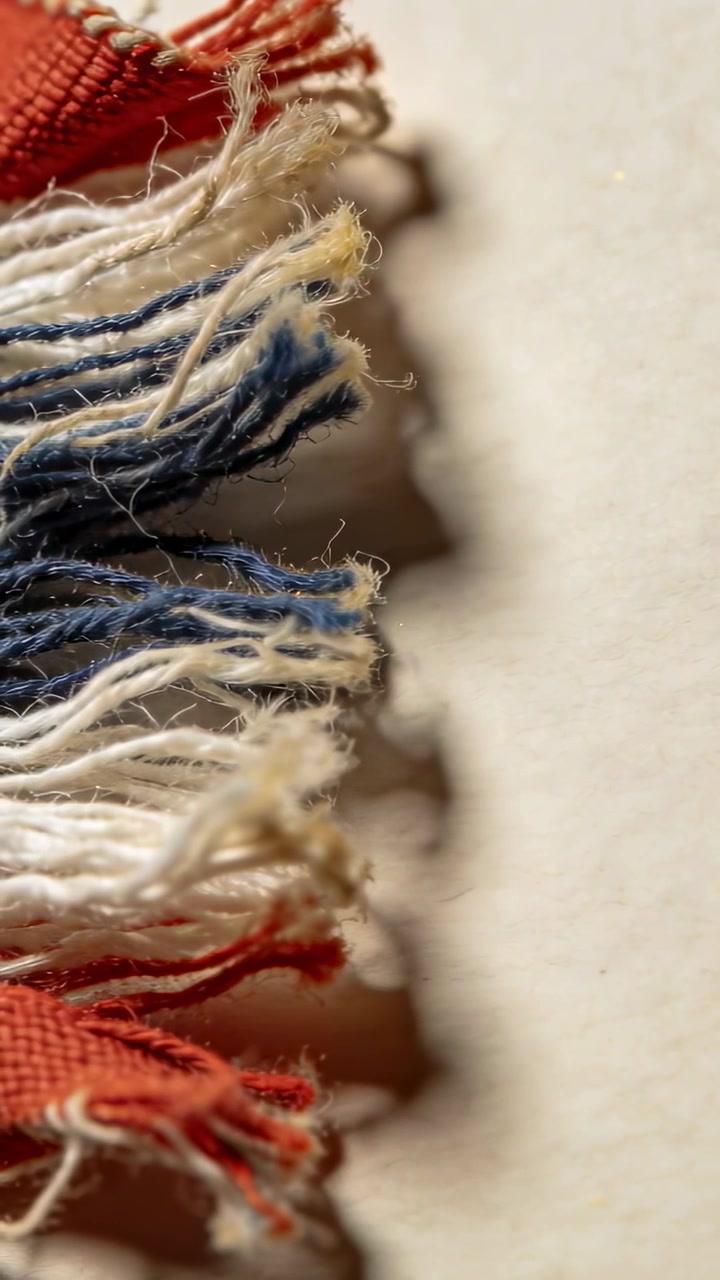 Vertical video: Tilting camera over frayed trim on table revealing red threads, copy space