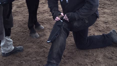 stunt man straps on protective gear as horse stands nearby