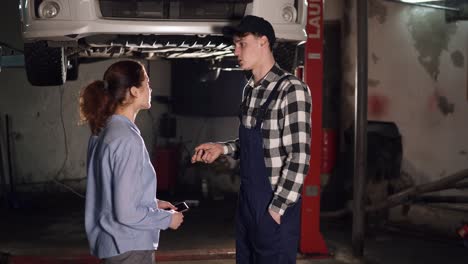 worker helps feminine client with vehicle and checks technical condition auto in car service