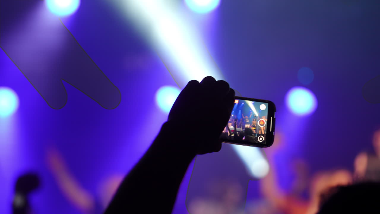 Hand holding a smartphone captures vibrant live music concert with colorful stage lights and enthusiastic fans cheering in the background, conveying event excitement