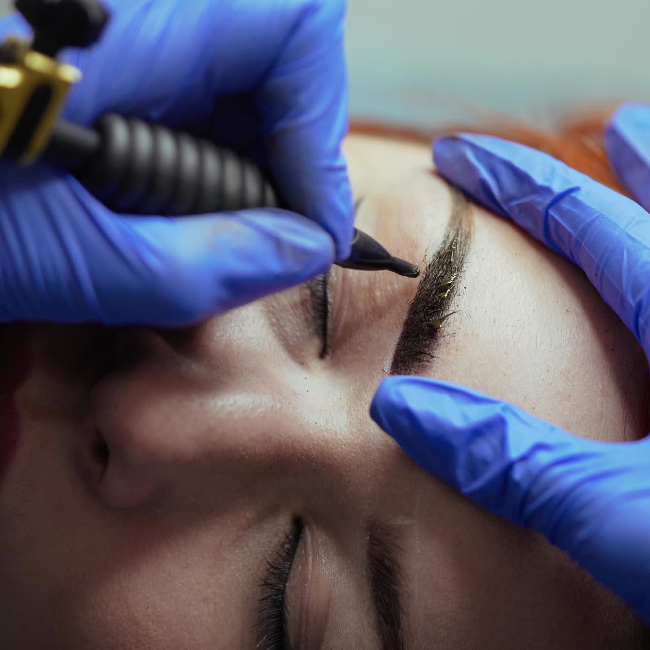 A beauty master is performing tattooing eyebrows in gloves for woman in the cosmetology. Close-up