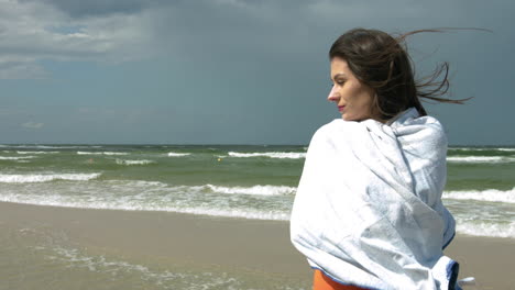 brunette girl at beach coming from cold ocean,wrapping in towel during windy day