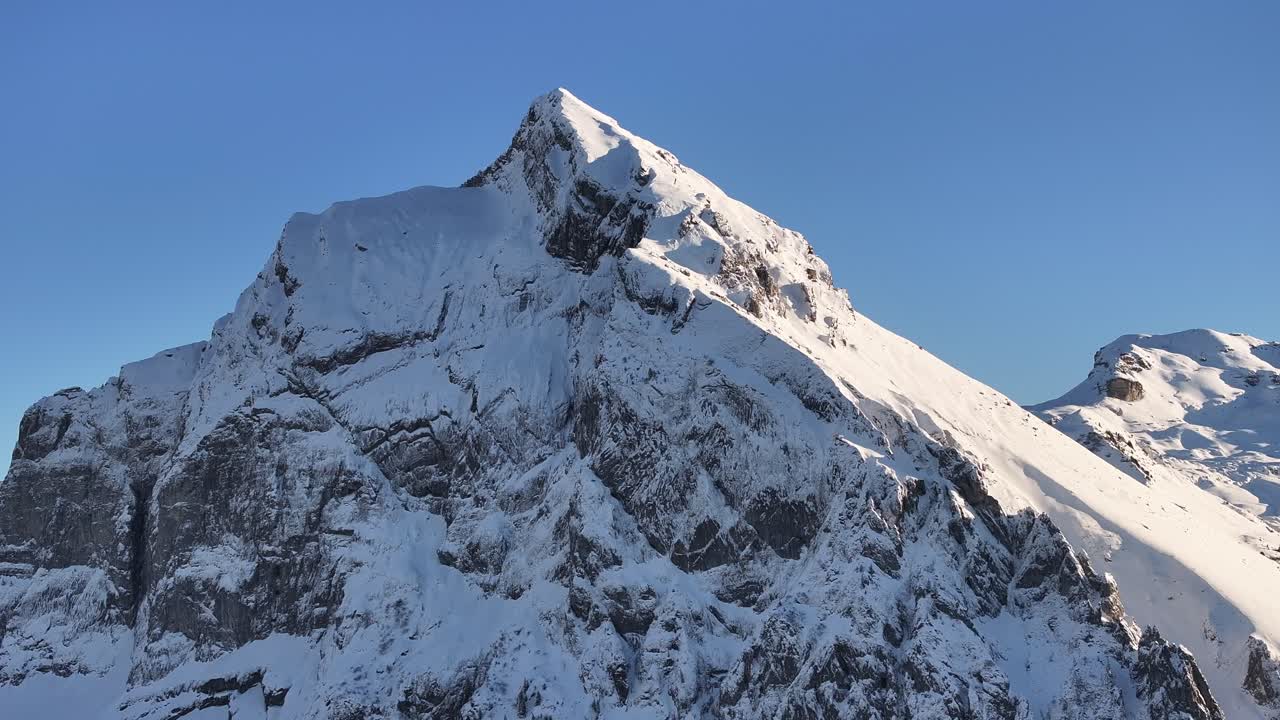 Close-up aerial view of the snow-covered summit of Fronalpstock mountain on a sunny day in the Swiss Alps.