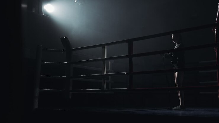 Pugile in piedi in un ring da boxe illuminato da un riflettore