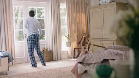 funny african american man dancing in bedroom having fun celebrating feeling positive enjoying successful lifestyle doing silly dance at home on weekend morning wearing pajamas