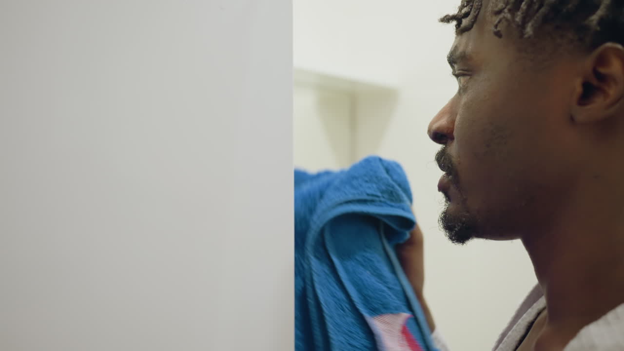 Immigrant man in robe stands in bathroom, facing mirror or wall, with focused expression. Clean, bright, minimalistic bathroom setting, peaceful atmosphere, with natural light from window