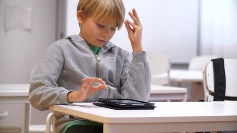 schoolboy in classroom at desk studying with tablet, pan medium shot