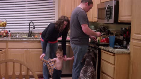 a father makes dinner while a mother undresses their little boy