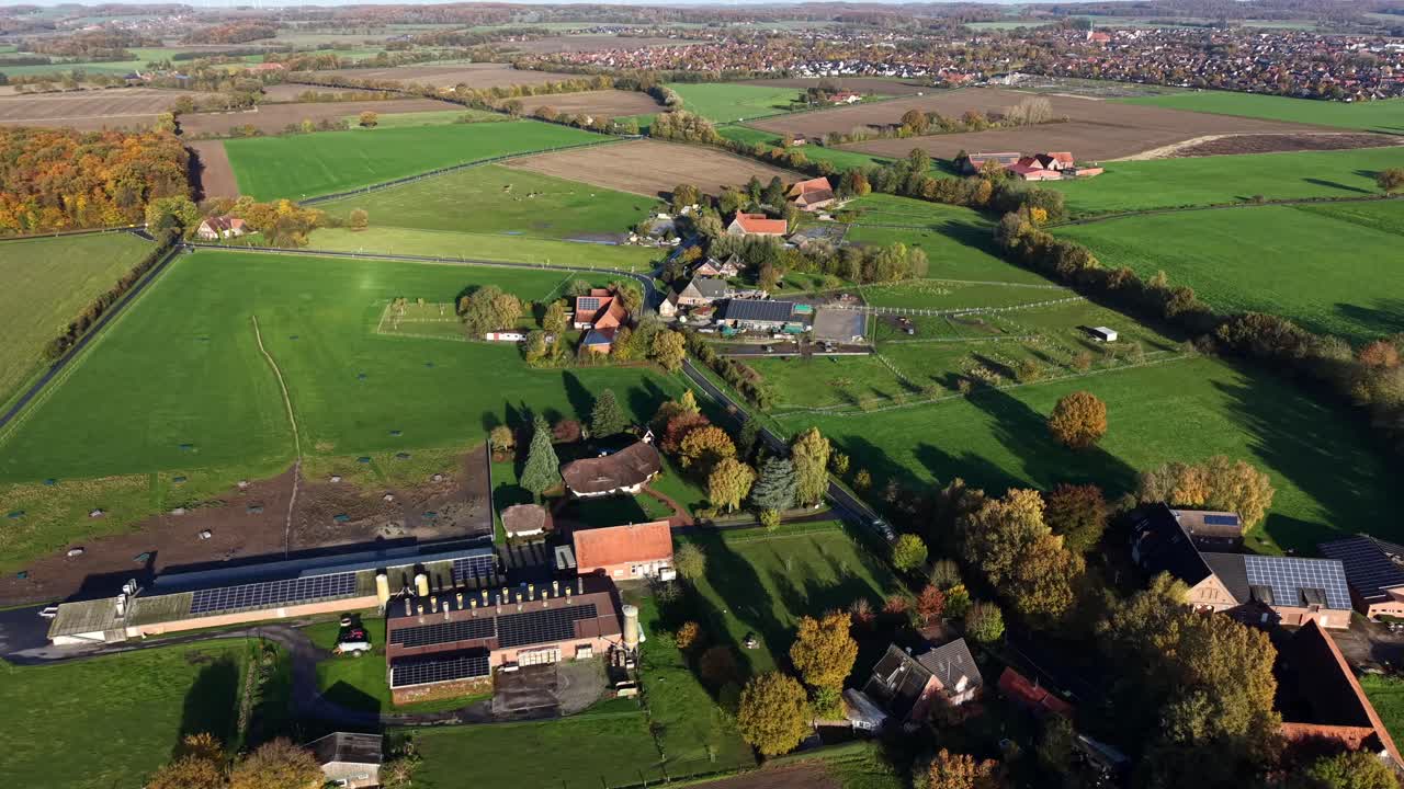 Vibrant colors of German countryside in fall season. Barn and farmstead with solar panels on roof. Colored trees and forest in suburbia. Sunny day in autumn. Peaceful scene. Aerial wide shot