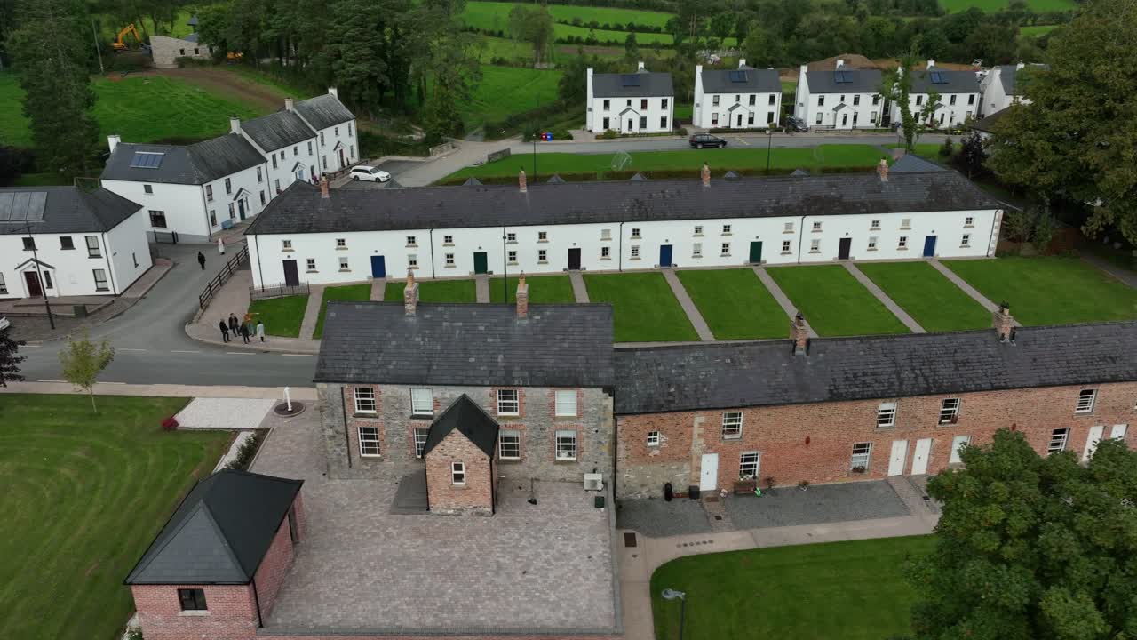 Mullan Village, County Monaghan, Ireland, September 2022. Drone orbits clockwise around a terrace of charming white houses with tidy lawns on a main road close to the border with Northern Ireland.