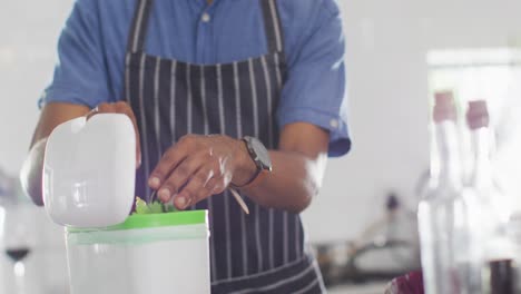 Midsection-of-african-american-man-composting-waste-in-kitchen