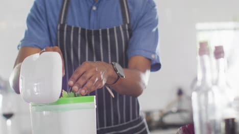 sección media de un hombre afroamericano compostando residuos en la cocina