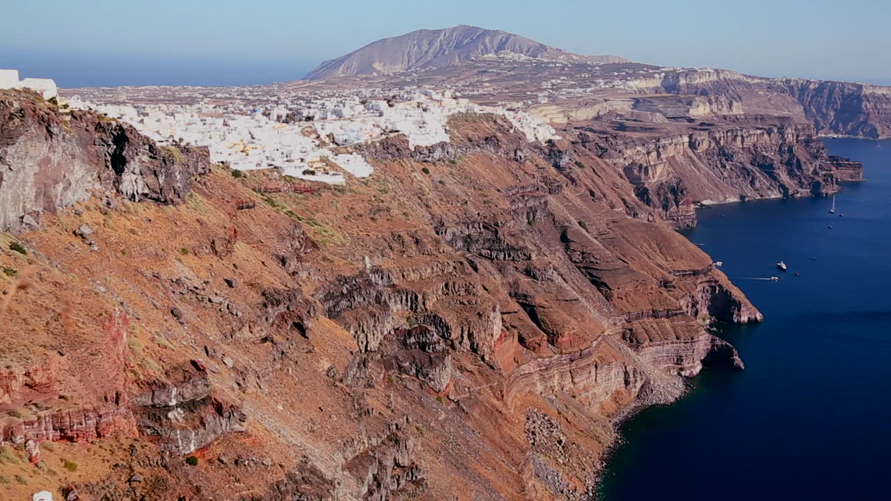 casas bordean las laderas de la isla griega de santorini con una bandera griega en la distancia